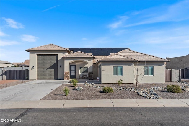 view of front facade with fence, stucco siding, concrete driveway, a tile roof, and roof mounted solar panels