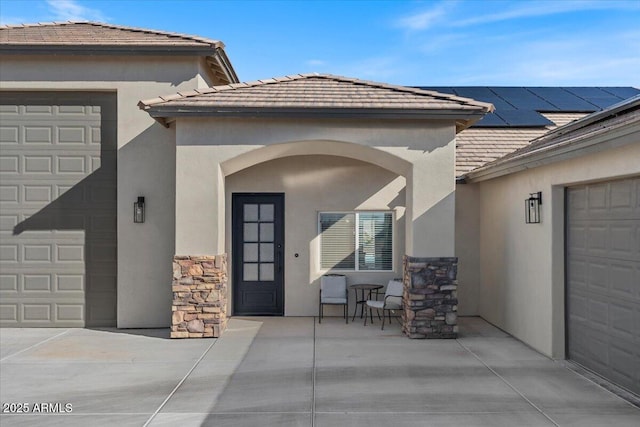 entrance to property with solar panels, a garage, stone siding, and stucco siding