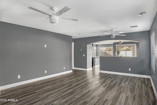 interior space with arched walkways, visible vents, dark wood-type flooring, and a ceiling fan