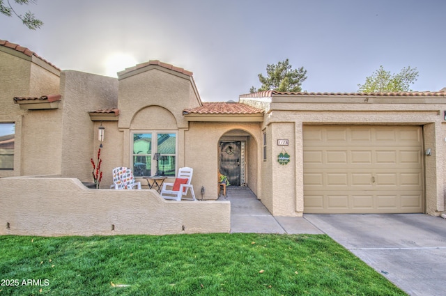 mediterranean / spanish-style home featuring an attached garage, a tile roof, driveway, stucco siding, and a front yard