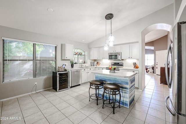 kitchen with appliances with stainless steel finishes, decorative light fixtures, vaulted ceiling, white cabinets, and a center island