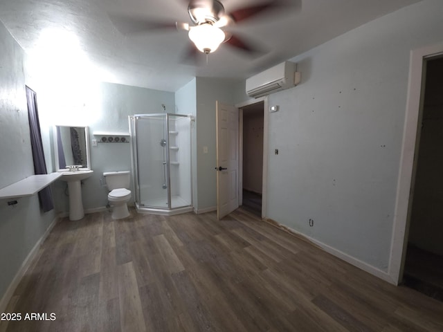 bathroom with hardwood / wood-style flooring, ceiling fan, toilet, a shower with shower door, and a wall unit AC