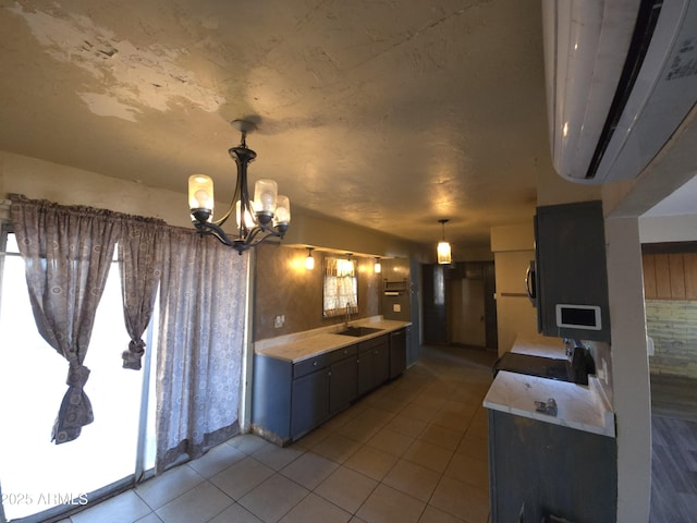 kitchen with sink, hanging light fixtures, an inviting chandelier, a wall unit AC, and light tile patterned floors