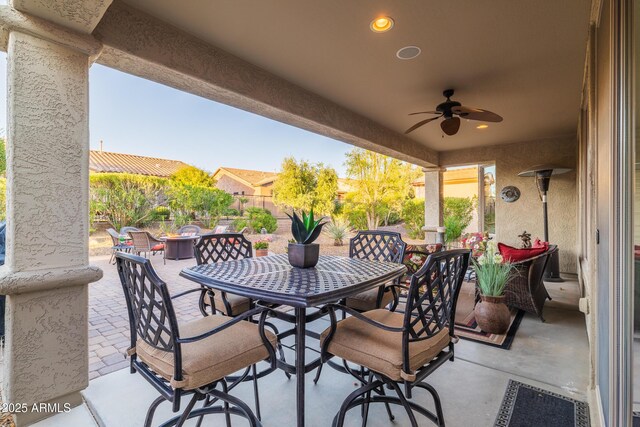 view of patio with outdoor dining space, a ceiling fan, fence, and an outdoor fire pit