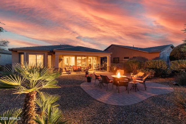 back of property at dusk with stucco siding, a patio, a fire pit, and fence