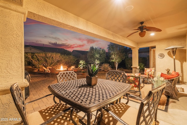 patio terrace at dusk with outdoor dining area and a ceiling fan