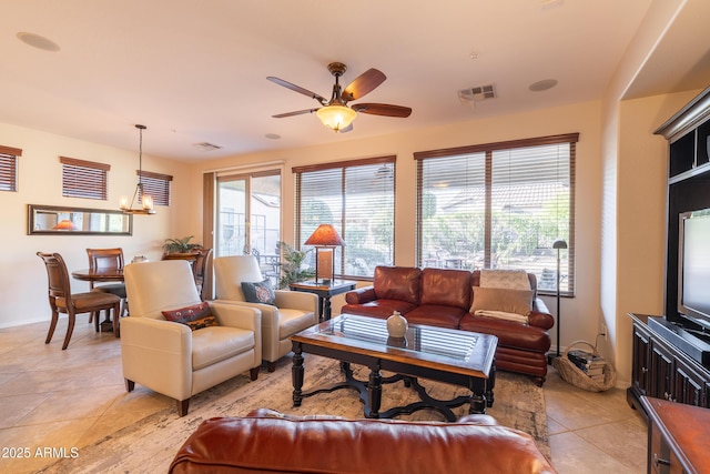 living room with light tile patterned floors, ceiling fan with notable chandelier, visible vents, and baseboards