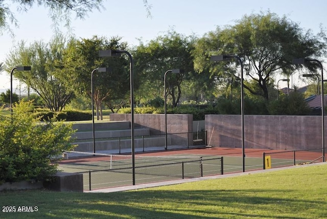 view of tennis court featuring a lawn and fence