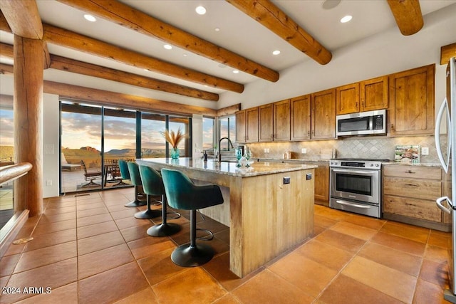 kitchen with stainless steel appliances, tasteful backsplash, light stone countertops, an island with sink, and a kitchen bar