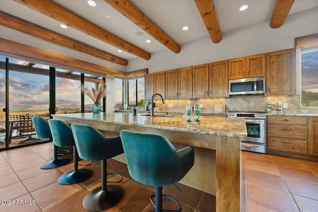 kitchen with sink, decorative backsplash, stainless steel appliances, and a large island with sink