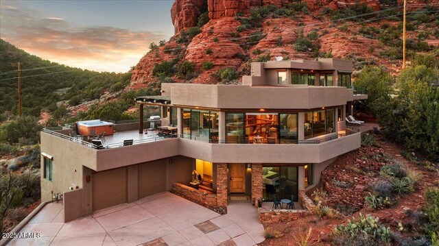 patio terrace at dusk with a mountain view, an outdoor living space with a fire pit, a grill, and a hot tub