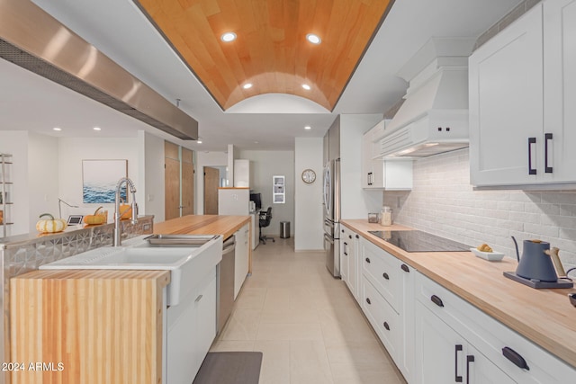 kitchen featuring decorative backsplash, custom exhaust hood, stainless steel appliances, white cabinets, and butcher block countertops