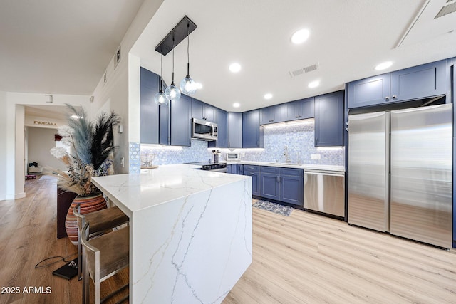 15225 N 100th St Unit 1185, Scottsdale, AZ 85260 - kitchen with stainless steel appliances, a peninsula, light stone countertops, light wood finished floors, and hanging light fixtures
