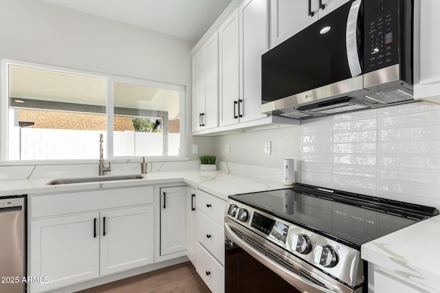 kitchen with light stone counters, white cabinets, stainless steel appliances, and a sink