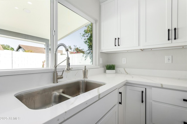 kitchen with a sink, light stone countertops, and white cabinetry