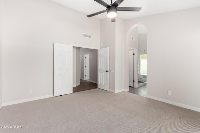 unfurnished bedroom with arched walkways, visible vents, carpet flooring, and baseboards