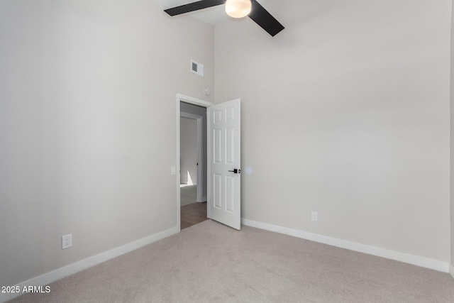 empty room featuring baseboards, visible vents, a high ceiling, ceiling fan, and light carpet