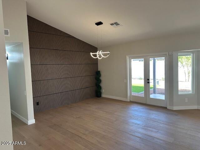 unfurnished dining area featuring visible vents, a notable chandelier, wood finished floors, and vaulted ceiling
