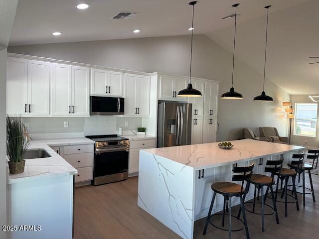 kitchen featuring visible vents, a kitchen island, decorative light fixtures, white cabinets, and stainless steel appliances