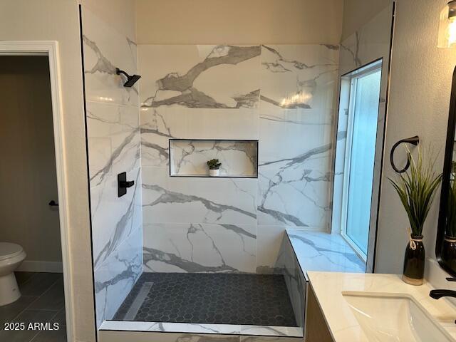 bathroom with a marble finish shower, toilet, vanity, and baseboards