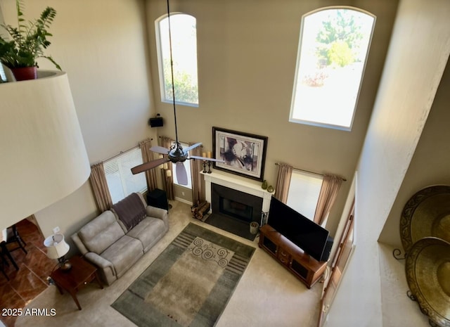 living room with a fireplace with flush hearth, a ceiling fan, and a towering ceiling