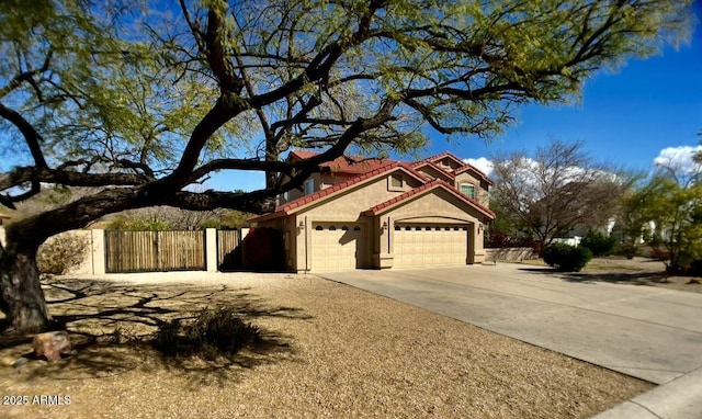 view of front of house with fence, concrete driveway, a tile roof, stucco siding, and a garage