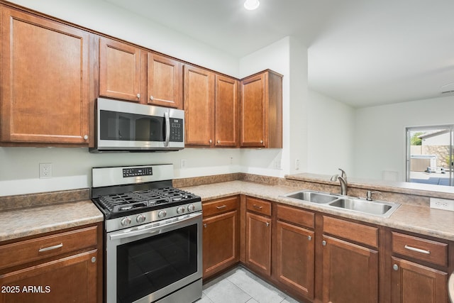 kitchen with brown cabinets, stainless steel appliances, a sink, and light tile patterned flooring