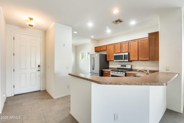 kitchen featuring recessed lighting, stainless steel appliances, a sink, visible vents, and brown cabinets