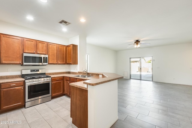 kitchen featuring visible vents, brown cabinetry, a peninsula, stainless steel appliances, and a sink