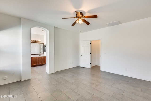 unfurnished room featuring baseboards, visible vents, arched walkways, ceiling fan, and a sink