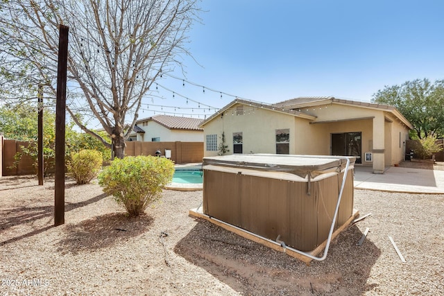 rear view of property with stucco siding, a hot tub, a fenced backyard, and a patio