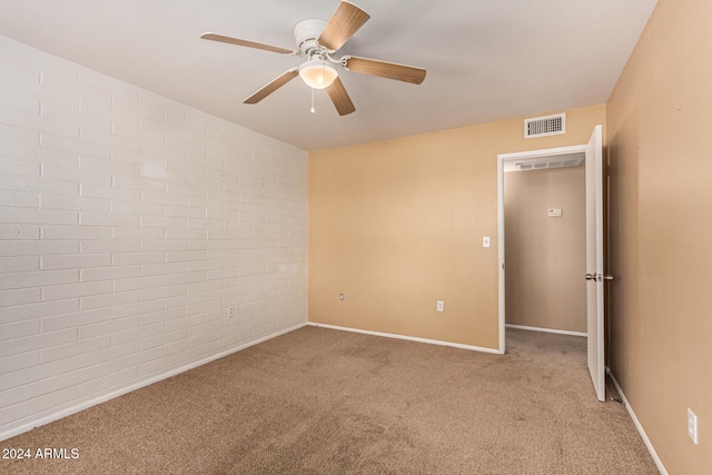 carpeted spare room featuring ceiling fan and brick wall