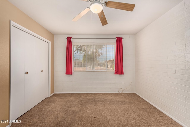 unfurnished bedroom featuring ceiling fan, a closet, carpet floors, and brick wall