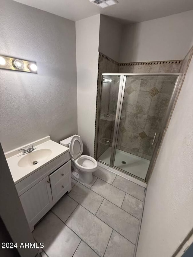 bathroom featuring toilet, vanity, tile patterned floors, and a shower with shower door