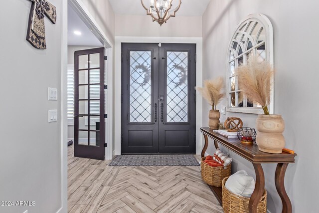 entrance foyer with a chandelier, light parquet flooring, and french doors