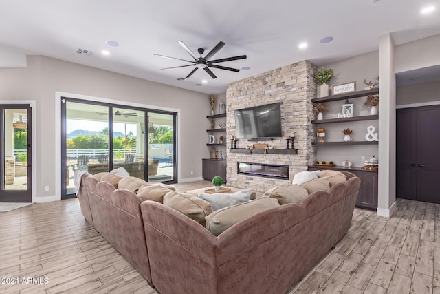 living room with light hardwood / wood-style floors, a stone fireplace, and ceiling fan