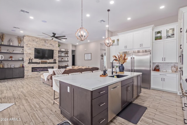 kitchen featuring white cabinets, appliances with stainless steel finishes, ceiling fan with notable chandelier, and a fireplace