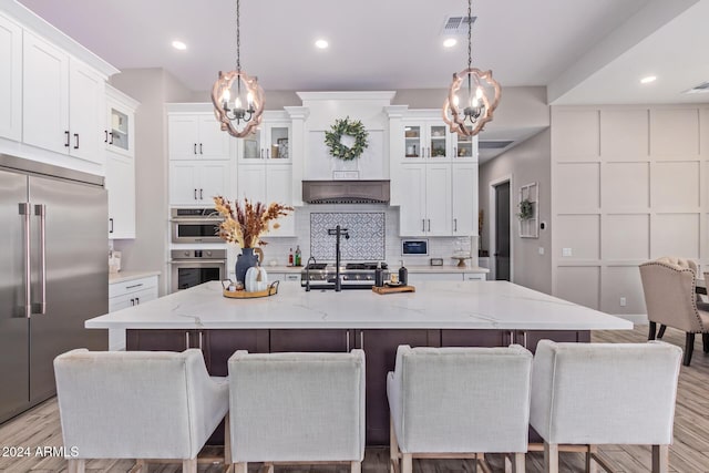 kitchen with stainless steel appliances, light hardwood / wood-style flooring, hanging light fixtures, and an island with sink