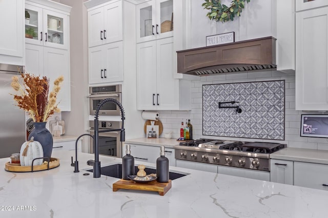 kitchen with white cabinetry, decorative backsplash, light stone countertops, and stainless steel appliances