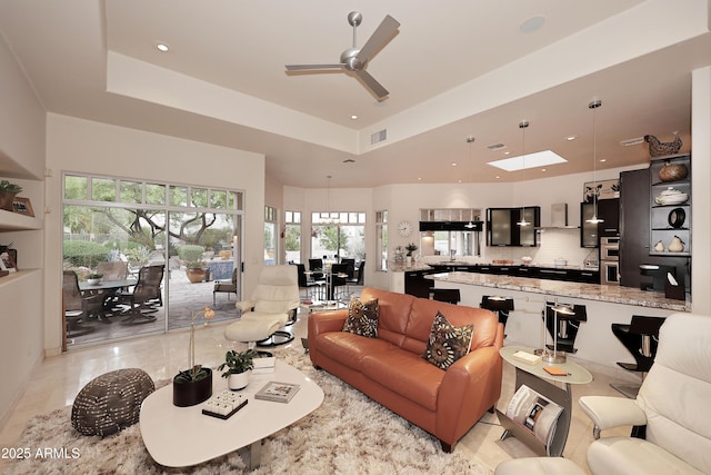 living room with plenty of natural light, visible vents, a raised ceiling, and ceiling fan
