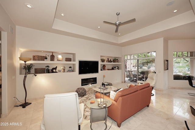 living area featuring built in shelves, a raised ceiling, ceiling fan, and recessed lighting