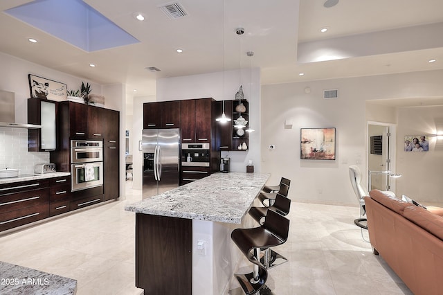 kitchen with a breakfast bar, visible vents, a peninsula, decorative backsplash, and appliances with stainless steel finishes