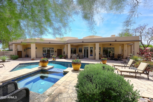 rear view of property with a ceiling fan, a patio, an outdoor pool, stucco siding, and an in ground hot tub
