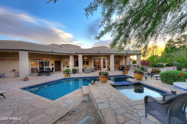 pool at dusk with an in ground hot tub, a patio, outdoor dining space, and an outdoor pool