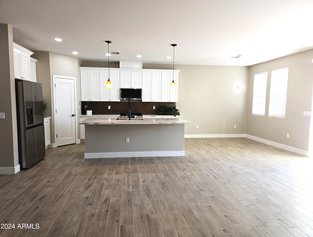 kitchen featuring white cabinets, an island with sink, hardwood / wood-style flooring, pendant lighting, and stainless steel appliances