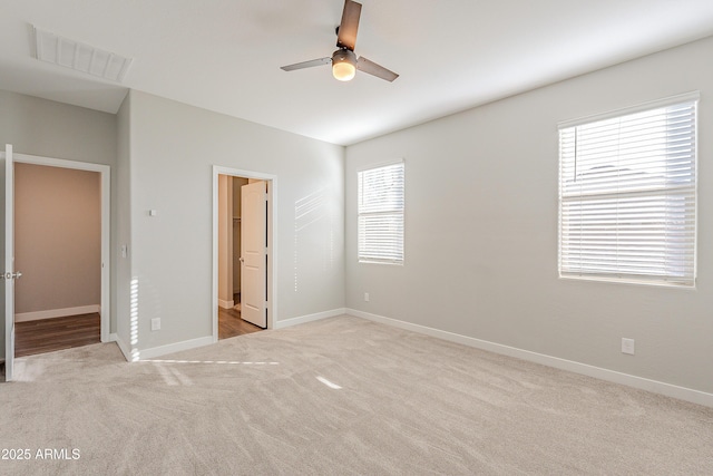 unfurnished bedroom with light carpet, a spacious closet, ceiling fan, ensuite bath, and a closet