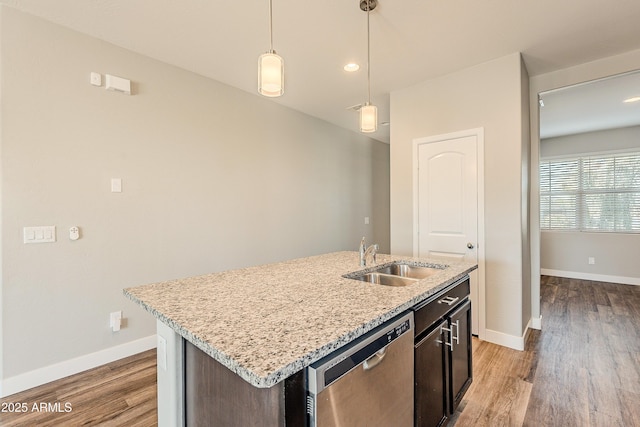 kitchen featuring decorative light fixtures, stainless steel dishwasher, sink, light stone countertops, and an island with sink