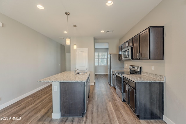 kitchen with light stone countertops, appliances with stainless steel finishes, dark brown cabinetry, sink, and hanging light fixtures