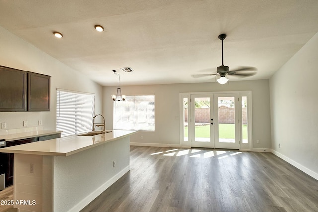 kitchen with light countertops, visible vents, a kitchen island with sink, a sink, and dark brown cabinetry