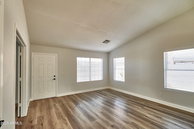 spare room with baseboards, visible vents, vaulted ceiling, and wood finished floors